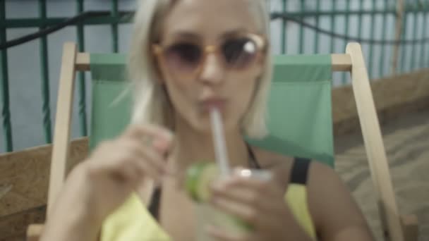 Ung söt blond flicka avkopplande utomhus med en kall drink. — Stockvideo