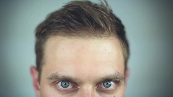 Close-up of a young green big eyed man raising eyebrow over grey background — Stock Video