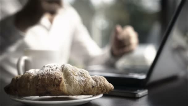 Uomo d'affari che prepara il tè mentre lavora alla scrivania con croissant per la colazione — Video Stock