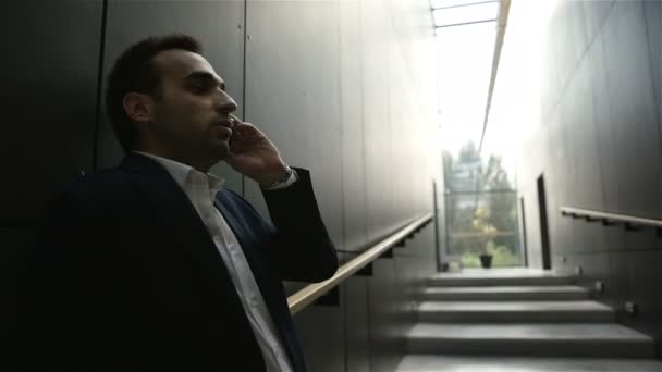 Businessman standing inside the building and talking by mobile phone — Stock Video