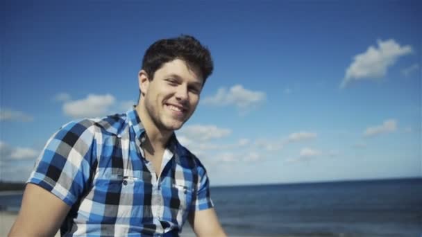 Handsome young man in casual checkered shirt against bright beach background — Stock Video