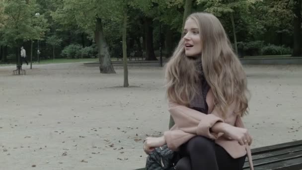 Una mujer bonita sentada en un banco en un parque esperando a alguien. Primer plano. . — Vídeo de stock