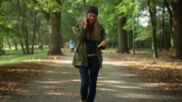 魅力的な若い女性の美しい秋の公園で携帯電話で話しています。. — ストック動画