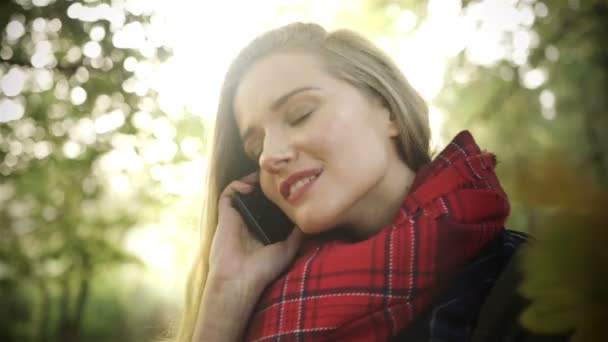 Mujer joven y feliz hablando por teléfono móvil en el parque de otoño . — Vídeo de stock