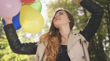 Sonbahar parkta gülümseyen renkli balonlar ile neşeli esmer kız.