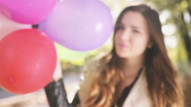 Веселая брюнетка с красочными воздушными шарами улыбается в осеннем парке . — стоковое видео