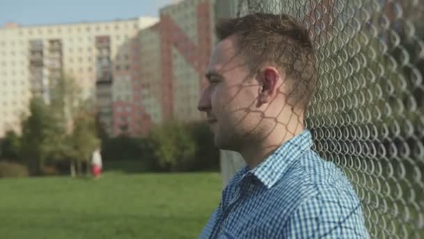 Beau homme souriant contre un mur de clôture moderne, extérieur . — Video