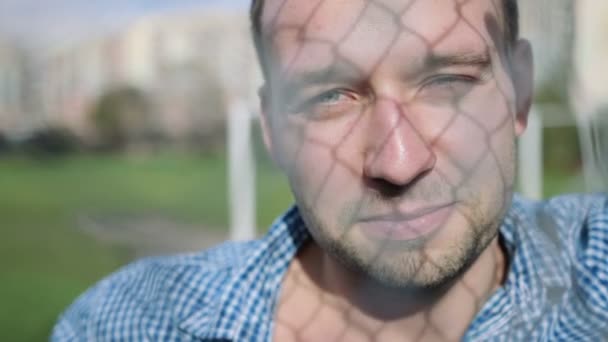 Handsome man smiling against a modern fence wall, outdoor. — Stock Video