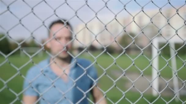 Handsome man smiling against a modern fence wall, outdoor. — Stock Video