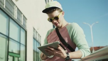 Genç şık genç bir şehirde güneşli gün boyunca sokak tablet kullanma.