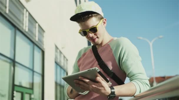 Молодий стильний підліток використовує планшет на вулиці міста під час сонячного дня . — стокове відео