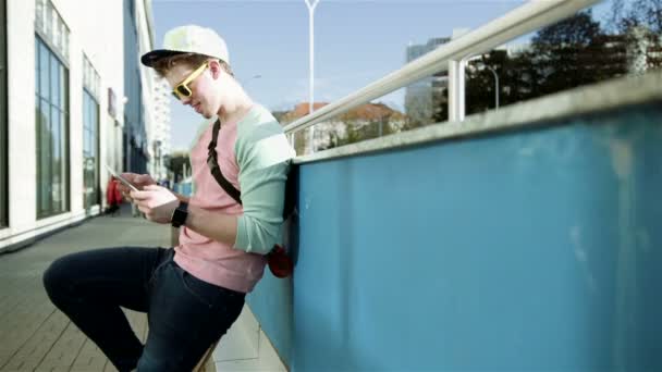 Young stylish teenager using tablet in a city street during sunny day.