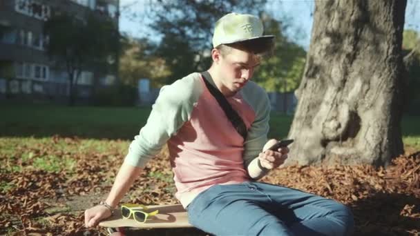 Vrolijke jongeman met een slimme telefoon in herfst park. — Stockvideo