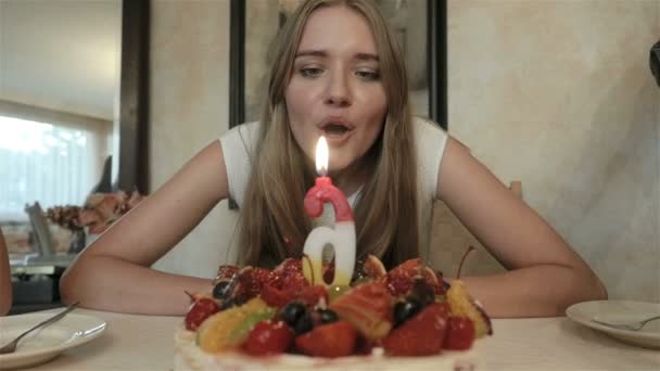 Retrato de una linda joven sentada frente al pastel de cumpleaños en casa . — Vídeo de stock