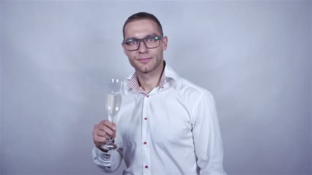 Mladý pohledný muž v bílé košili oslavit šampaňským šedé pozadí.