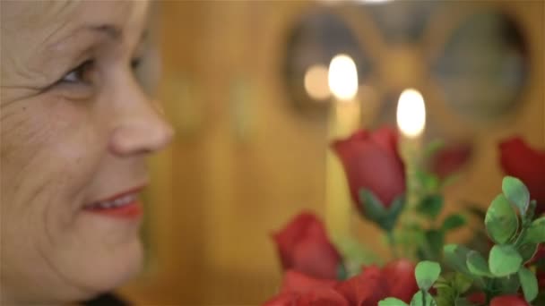 Zralá žena drží velkou kytici rudých růží a s úsměvem.