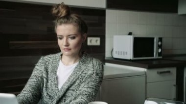 Dizüstü bilgisayar kullanan parlak mutfakta dalgın genç sarışın kadın.