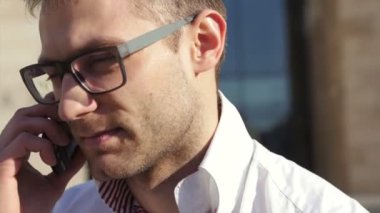 Mutlu genç işadamı ofisinin önünde oturan telefonda konuşuyor.