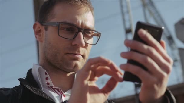 Porträtt av stilig ung man skicka ett textmeddelande när du står utanför. — Stockvideo