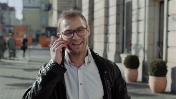 Pohledný mladý muž přichází a mluví po telefonu zpomaleně. — Stock video