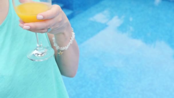 Kobieta pije sok pomarańczowy stojący w pobliżu basenu. — Wideo stockowe