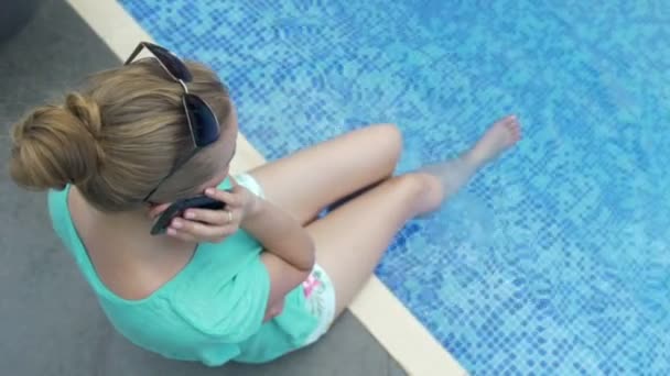 Mujer atractiva joven usando su teléfono celular en vacaciones cerca de la piscina . — Vídeo de stock
