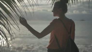 Yan bir tropik sahilde günbatımı ayakta bir genç kadının portresi.