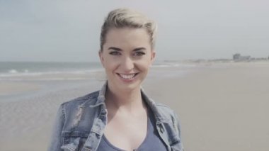 Denim ceket yalnız plajda kameraya gülümseyen mutlu genç kadın.