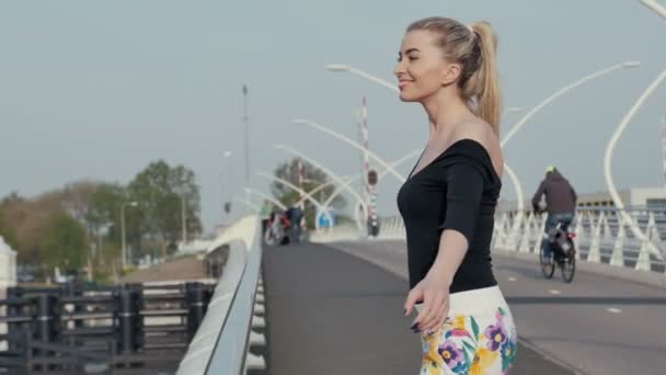 Vacker blond flicka står på bron. — Stockvideo