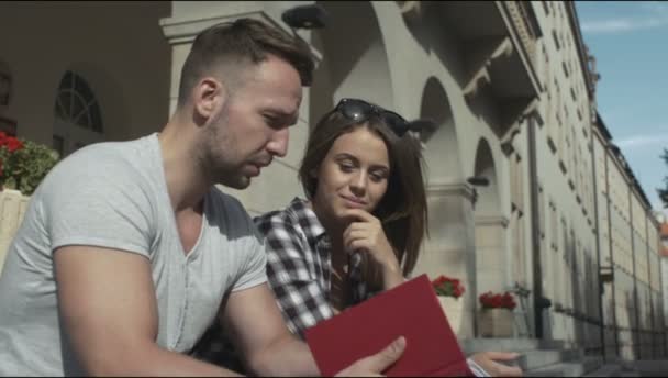 Jóvenes estudiantes leyendo un libro juntos frente a la Universidad . — Vídeos de Stock