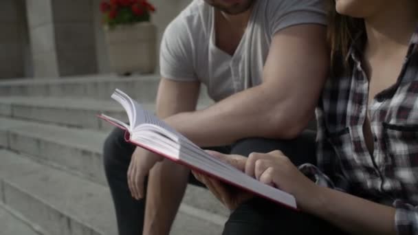 Jóvenes estudiantes leyendo un libro juntos frente a la Universidad . — Vídeo de stock