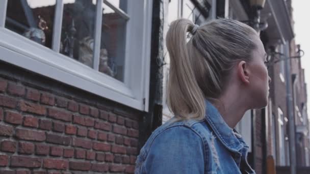 Jonge blonde vrouw te wachten voor iemand, buitenshuis. — Stockvideo