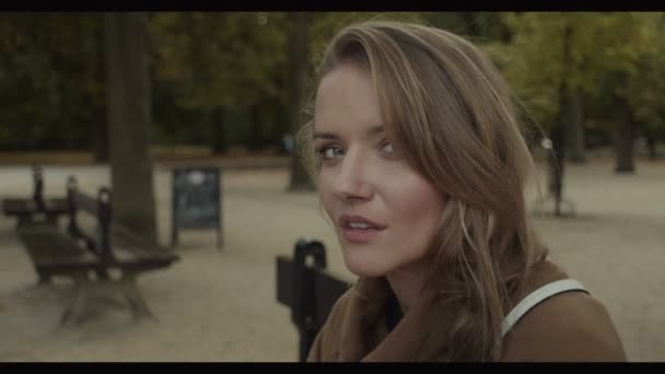Beautiful young woman sitting on a bench in autumn park. — Stock Video