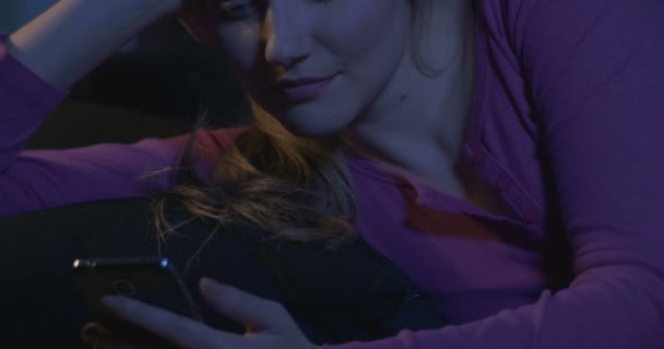 Aantrekkelijke jonge vrouw met behulp van smartphone liggend op sofa's nachts. — Stockvideo