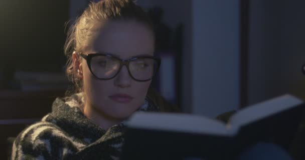 Jeune femme portant des lunettes de vue lisant un livre le soir . — Video