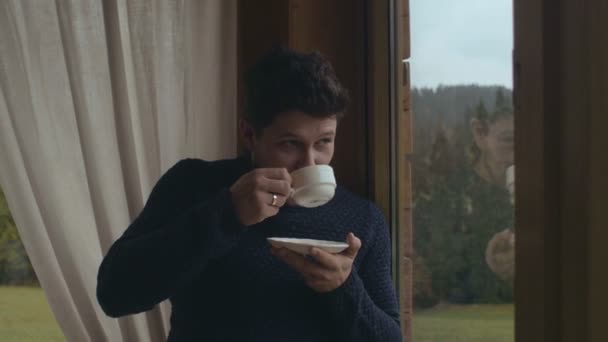 Joven bebiendo café en casa sentado cerca de una ventana . — Vídeo de stock