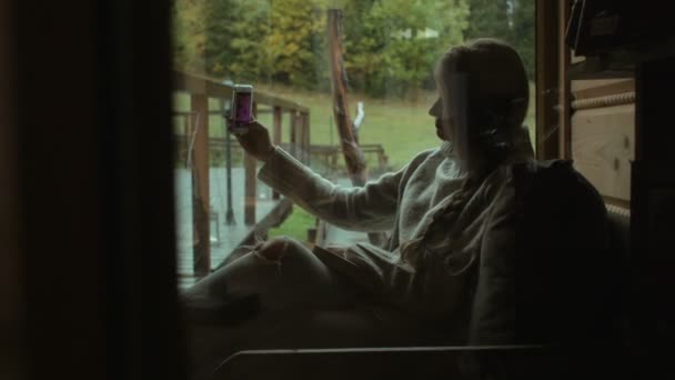 여자는 창 및 스마트폰으로 자신의 복용 사진 근처에 앉아. — 비디오