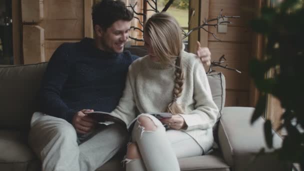 Young couple reading together a magazine in their living room at home. — Stock Video