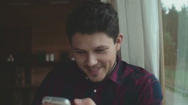 Oturma odasında smartphone kullanan genç adam.