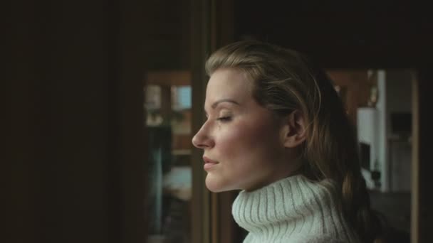 Vacker eftertänksam kvinna tittar genom ett fönster. — Stockvideo