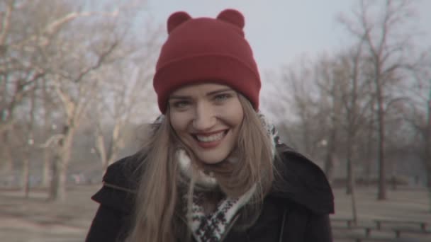 Mujer en sombrero rojo mirando a la cámara y sonriendo, al aire libre . — Vídeo de stock