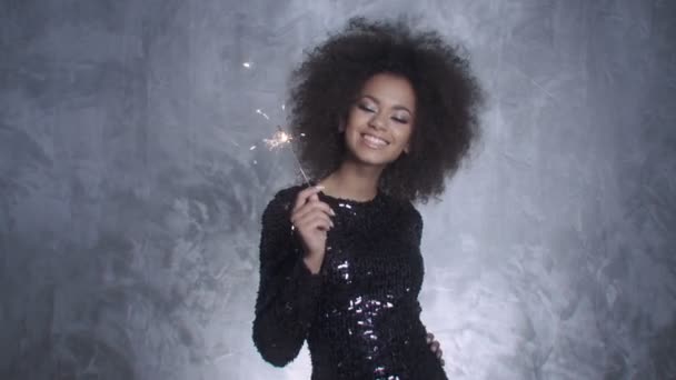 Jovem mulher elegante com afro segurando sparklers e sorrindo para uma câmera . — Vídeo de Stock