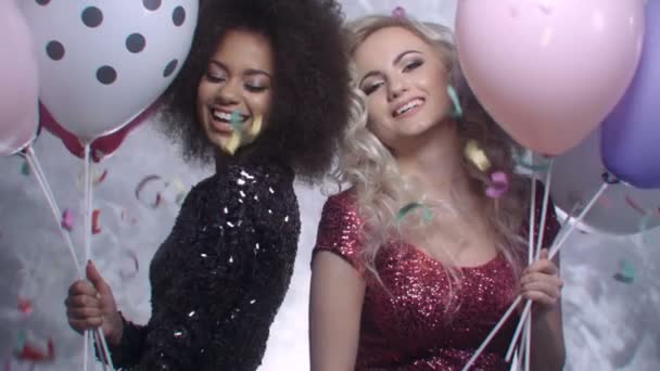 Twee sexy meisjes dansen onder kleurrijke confetti in studio. — Stockvideo