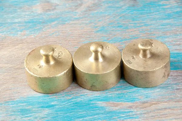 Three antique bronze weights for scales on blue wooden background. Copy space for text and food photography props.