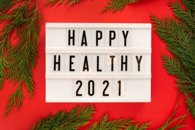 Mutlu Sağlıklı 2021 yılı, parlak kırmızı arka planda beyaz bir ışık kutusunda ardıç dallarıyla, düz bir zeminde sergilendi..