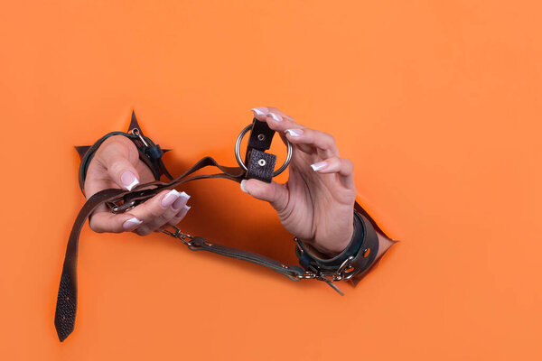 Adult sex toys, minimal design, isolated on an orange background. Women's hands in handcuffs. Bdsm.