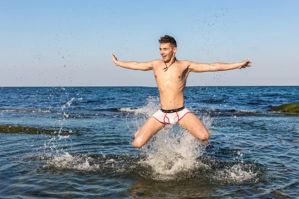 Naked young man jumping for joy from see water — Stock Photo, Image