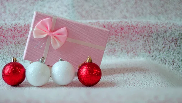 Yumuşak pembe renkli hediye kutusu ve kar taklidi yapan açık arkaplanda kırmızı ve gümüş renkli Noel topları. Boş alan. Noel arkaplanı, tatil kartı.