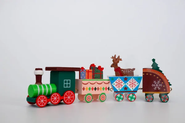 Eine hölzerne Spielzeugeisenbahn trägt die Attribute der Winterferien auf weißem Hintergrund. Image für ein dekoratives Weihnachtsfeiertagskonzept. Freiraum zum Kopieren. — Stockfoto