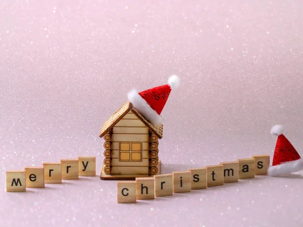 A toy house with a Christmas hat on the chimney and wooden blocks forming the expression: merry Christmas. Free space for copying